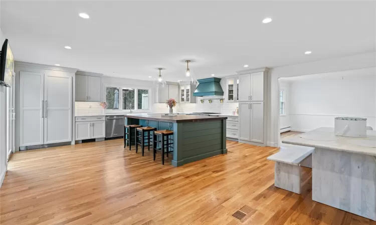 Kitchen featuring tasteful backsplash, premium range hood, a center island, light wood-type flooring, and appliances with stainless steel finishes