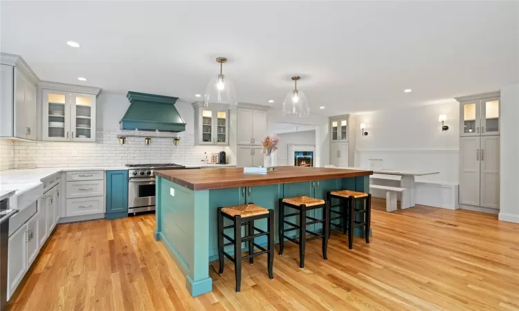 Kitchen with a kitchen bar, butcher block countertops, high end stove, custom range hood, and pendant lighting