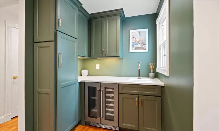 Bar featuring beverage cooler, light hardwood / wood-style flooring, light stone counters, and sink