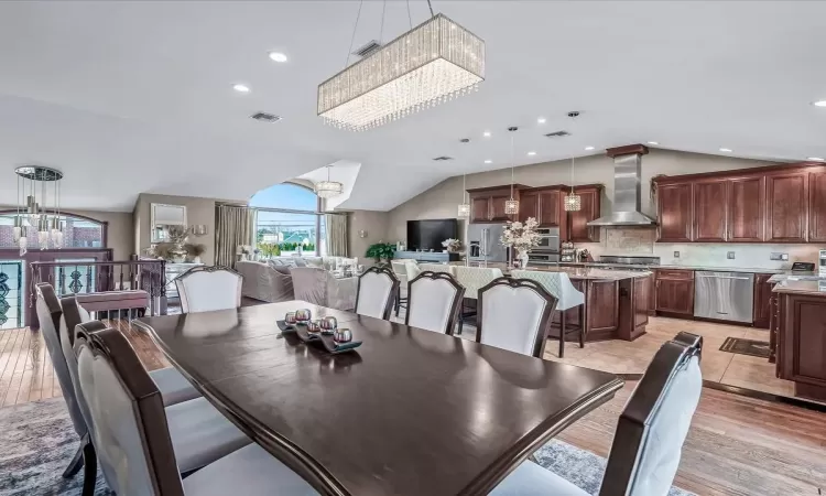 Kitchen featuring appliances with stainless steel finishes, a kitchen island with sink, hanging light fixtures, and wall chimney range hood