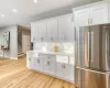 Kitchen featuring white cabinets, tasteful backsplash, stainless steel fridge, light wood-type flooring, and light stone counters