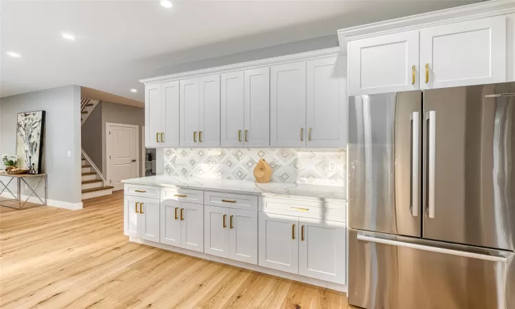 Kitchen featuring white cabinets, tasteful backsplash, stainless steel fridge, light wood-type flooring, and light stone counters