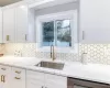 Kitchen with dishwashing machine, decorative backsplash, sink, and white cabinetry