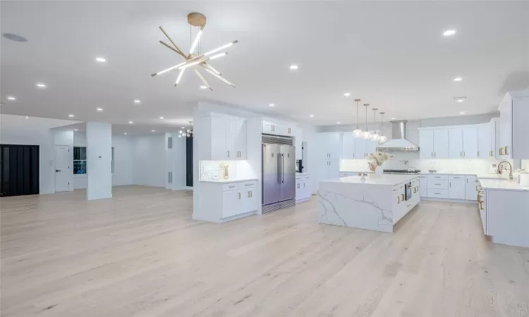 Kitchen featuring white cabinets, a kitchen island, wall chimney range hood, backsplash, and light hardwood / wood-style flooring