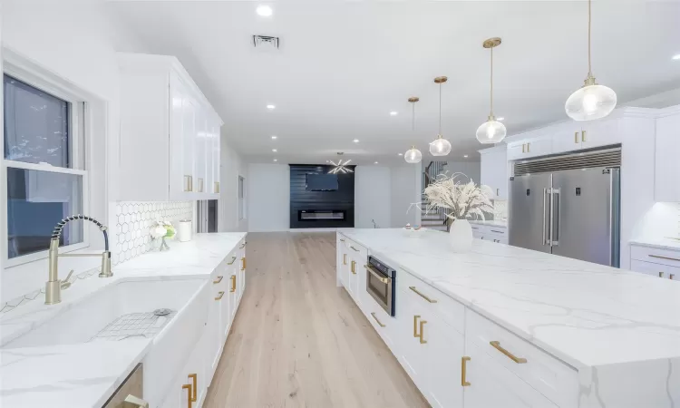 Kitchen featuring light stone countertops, decorative light fixtures, white cabinetry, stainless steel built in refrigerator, and decorative backsplash