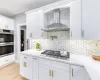 Kitchen with white cabinetry, appliances with stainless steel finishes, tasteful backsplash, and wall chimney range hood