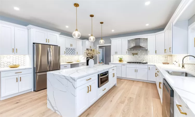 Kitchen featuring decorative light fixtures, sink, appliances with stainless steel finishes, white cabinets, and wall chimney exhaust hood