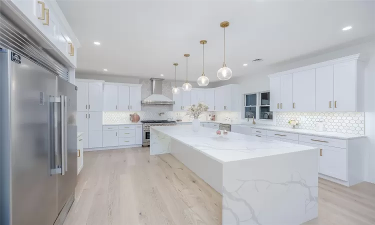 Kitchen with wall chimney range hood, high quality appliances, white cabinetry, and a center island