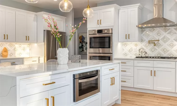 Kitchen with decorative backsplash, white cabinets, wall chimney exhaust hood, and stainless steel appliances