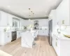 Kitchen with pendant lighting, a kitchen island with sink, stainless steel appliances, white cabinets, and wall chimney exhaust hood