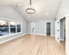 Unfurnished living room featuring vaulted ceiling, an inviting chandelier, and light hardwood / wood-style flooring