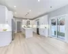 Kitchen with white cabinetry, appliances with stainless steel finishes, decorative light fixtures, a kitchen island, and light hardwood / wood-style flooring