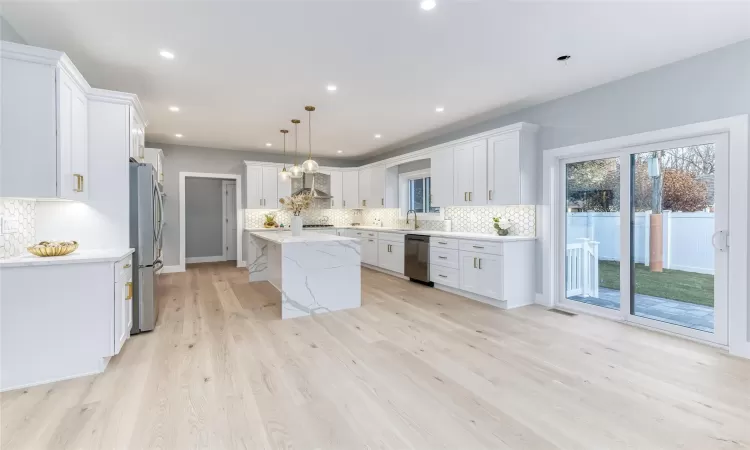 Kitchen with white cabinetry, appliances with stainless steel finishes, decorative light fixtures, a kitchen island, and light hardwood / wood-style flooring