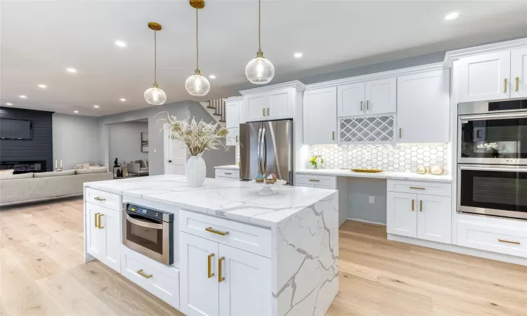 Kitchen featuring backsplash, pendant lighting, light hardwood / wood-style flooring, stainless steel appliances, and white cabinets