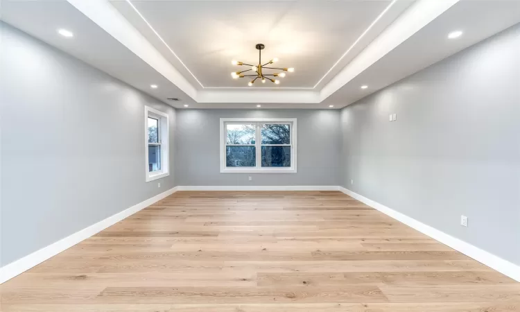 Unfurnished room featuring a raised ceiling, an inviting chandelier, and light hardwood / wood-style flooring