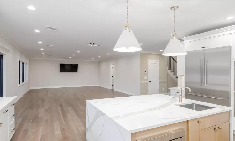 Kitchen featuring stainless steel built in refrigerator, sink, light stone countertops, ornamental molding, and a center island with sink