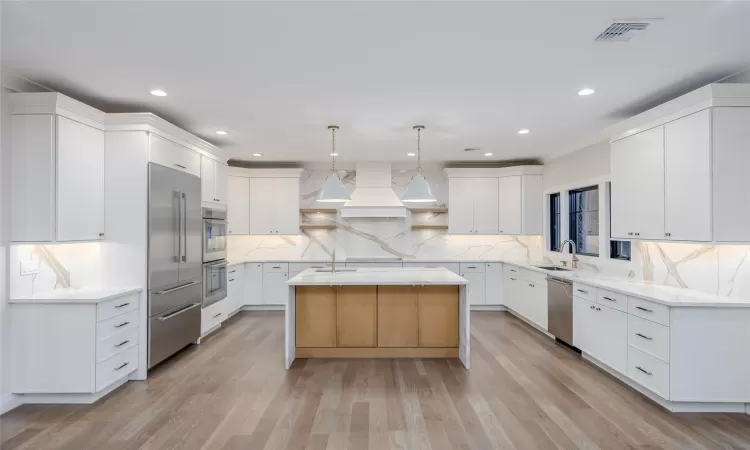 Kitchen with white cabinetry, pendant lighting, stainless steel appliances, and a center island with sink