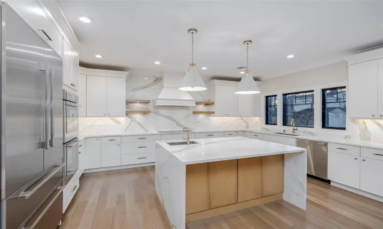 Kitchen featuring pendant lighting, custom exhaust hood, white cabinetry, stainless steel appliances, and a center island with sink