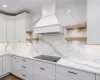 Kitchen with light stone counters, premium range hood, white cabinets, and black electric stovetop