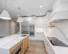 Kitchen featuring a center island with sink, pendant lighting, built in appliances, custom range hood, and white cabinets