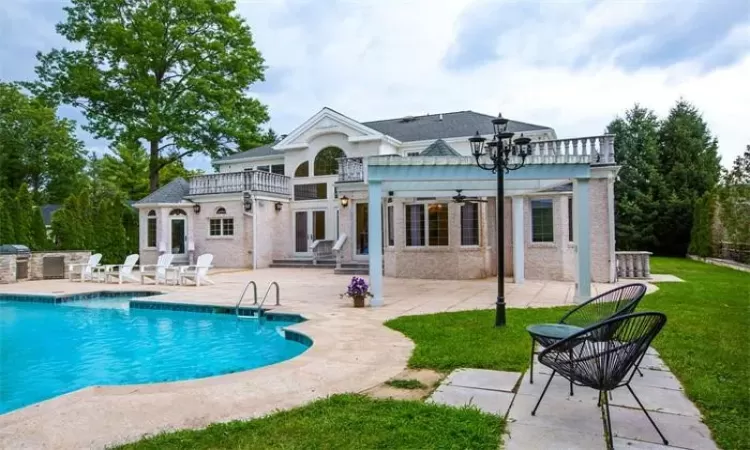 Back of house with area for grilling, a patio, a lawn, and a balcony