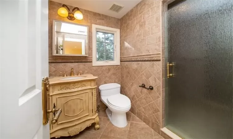 Bathroom with tile patterned flooring, vanity, tile walls, toilet, and walk in shower