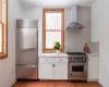 Kitchen featuring premium appliances, white cabinets, wall chimney exhaust hood, backsplash, and light hardwood / wood-style flooring