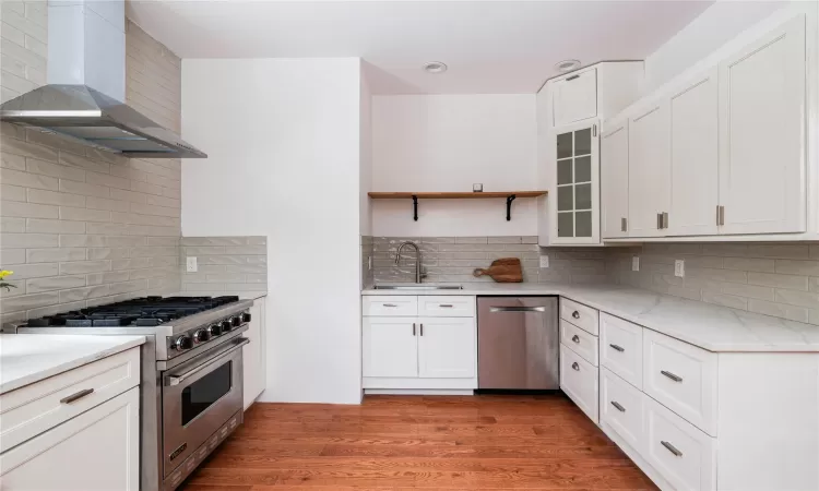 Kitchen with sink, wall chimney range hood, appliances with stainless steel finishes, and tasteful backsplash