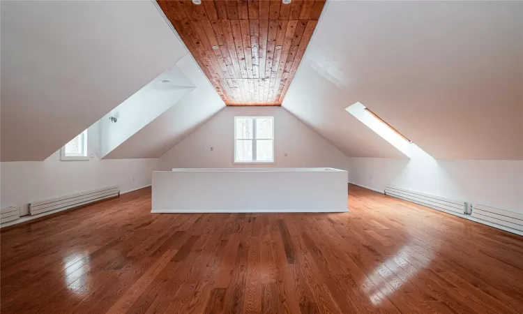 Additional living space featuring plenty of natural light, hardwood / wood-style floors, a baseboard heating unit, and vaulted ceiling