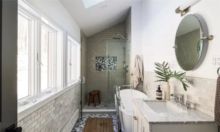 Bathroom featuring separate shower and tub, vanity, tile walls, vaulted ceiling with skylight, and tile patterned flooring