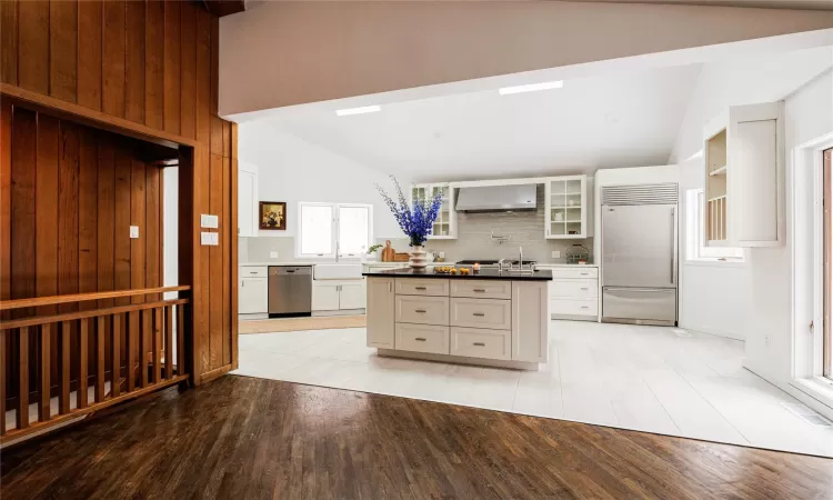 Kitchen featuring stainless steel appliances, white cabinets, backsplash, and wall chimney range hood