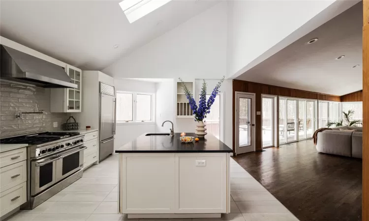 Kitchen with sink, a kitchen island with sink, premium appliances, high vaulted ceiling, and wall chimney exhaust hood