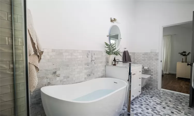 Bathroom featuring toilet, vanity, tile walls, and a bathing tub