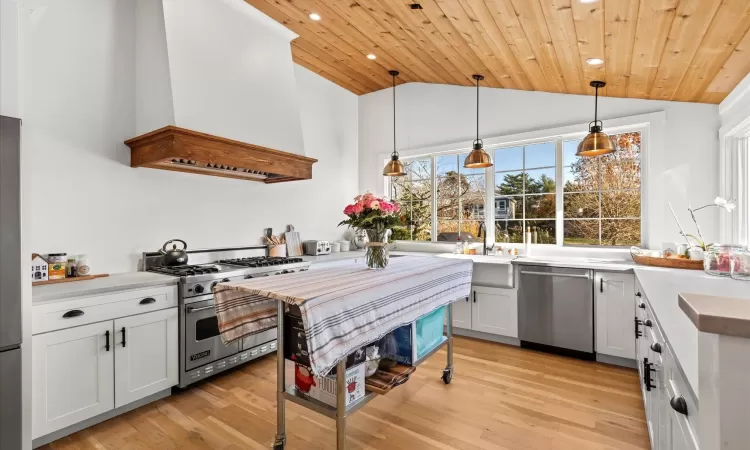 Kitchen with appliances with stainless steel finishes, wood ceiling, custom exhaust hood, decorative light fixtures, and white cabinetry