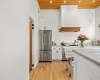 Kitchen featuring wooden ceiling, white cabinetry, custom range hood, and high end appliances