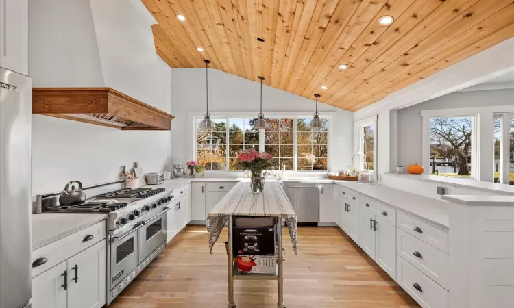 Kitchen featuring custom exhaust hood, appliances with stainless steel finishes, wooden ceiling, hanging light fixtures, and plenty of natural light