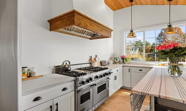 Kitchen with hanging light fixtures, custom exhaust hood, white cabinets, range with two ovens, and lofted ceiling