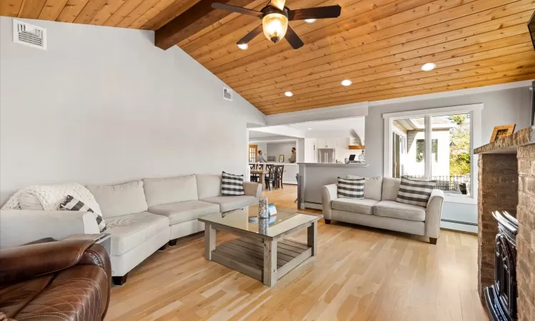 Living room featuring a baseboard radiator, wood ceiling, a fireplace, vaulted ceiling with beams, and light wood-type flooring