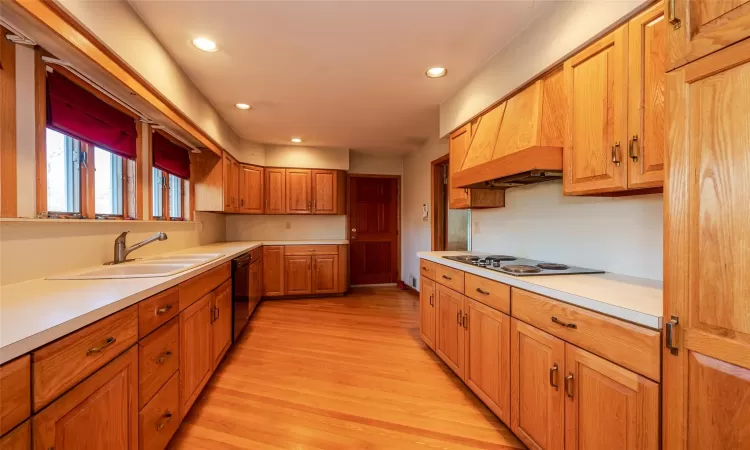 Kitchen with black appliances, light wood-type flooring, sink, and custom exhaust hood