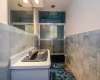 Bathroom with tile walls, combined bath / shower with glass door, vanity, and tile patterned flooring