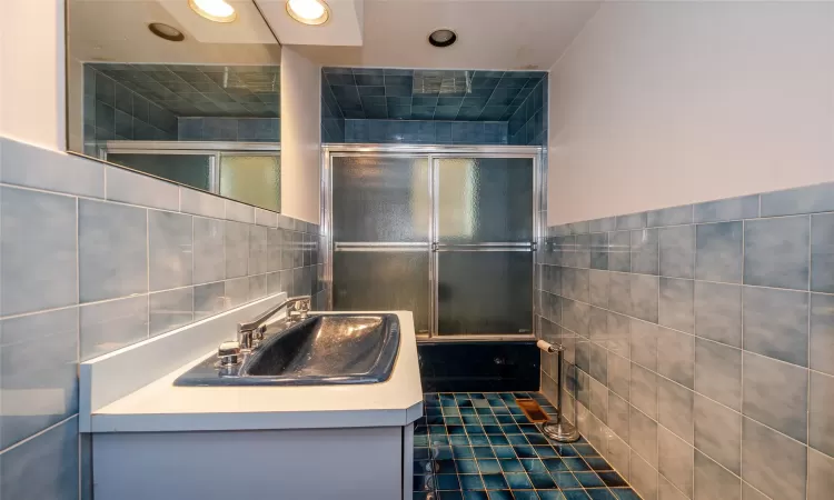 Bathroom with tile walls, combined bath / shower with glass door, vanity, and tile patterned flooring