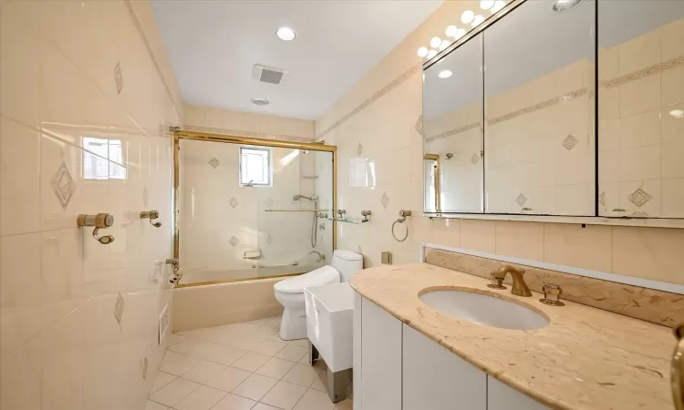 Full bathroom with tile patterned floors, tile walls, combined bath / shower with glass door, toilet, and vanity