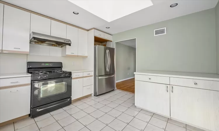 Kitchen featuring white cabinets, exhaust hood, a skylight, black gas range, and stainless steel refrigerator