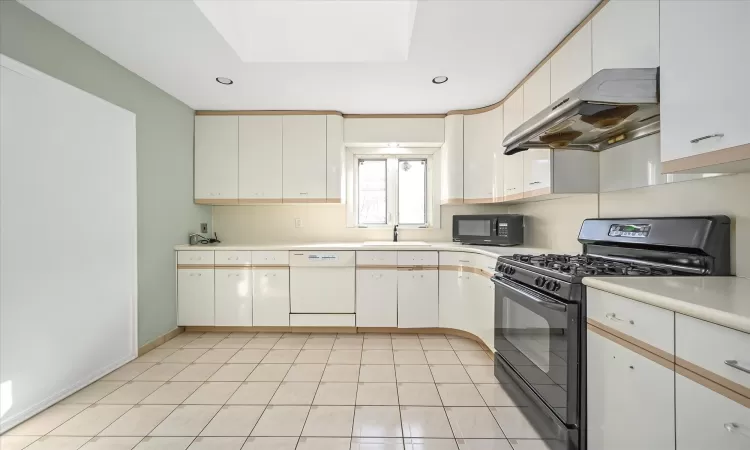 Kitchen featuring sink, light tile patterned flooring, black appliances, and white cabinets