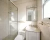 Bathroom featuring toilet, vanity, an enclosed shower, and tile walls