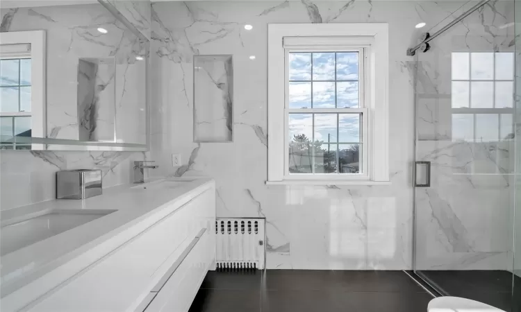 Bathroom featuring a shower with shower door, vanity, and radiator heating unit