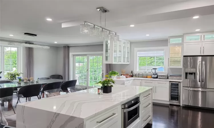 Kitchen with appliances with stainless steel finishes, decorative light fixtures, white cabinetry, wine cooler, and light stone counters