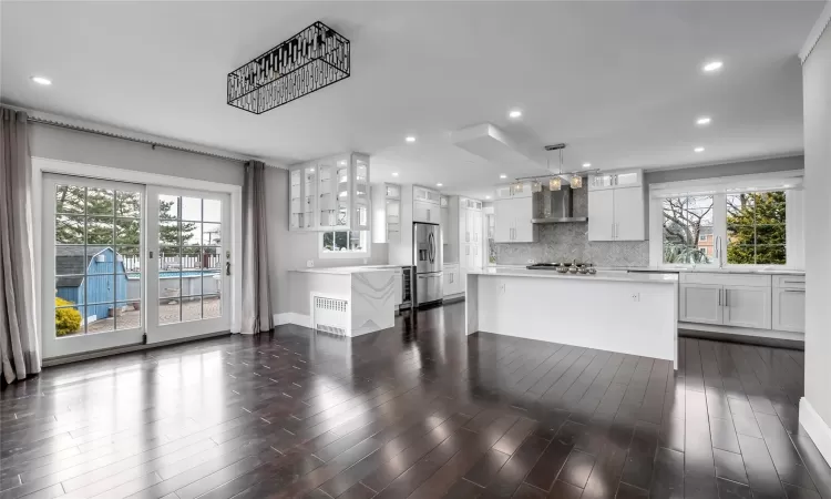 Kitchen featuring white cabinets, wall chimney exhaust hood, a kitchen island, decorative light fixtures, and stainless steel appliances