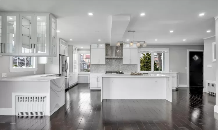 Kitchen with radiator, white cabinets, hanging light fixtures, and stainless steel fridge