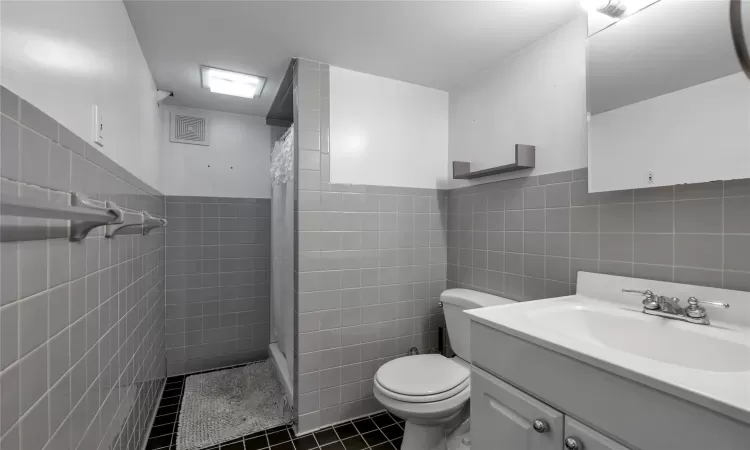 Bathroom with curtained shower, tile patterned floors, vanity, tile walls, and toilet